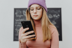 Mädchen mit Handy, Quelle: Pexels | Carolina Krabowska Jugendliches Mädchen steht vor Tafel und schaut auf ihr Handy